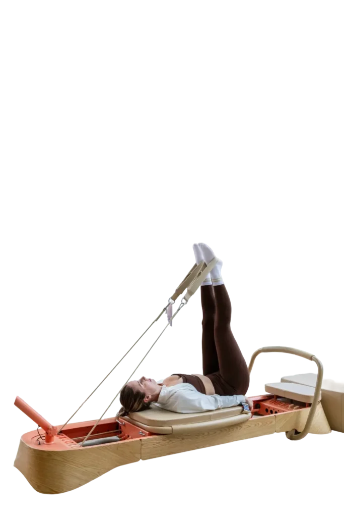A member lying on the reformer with both legs raised in the straps