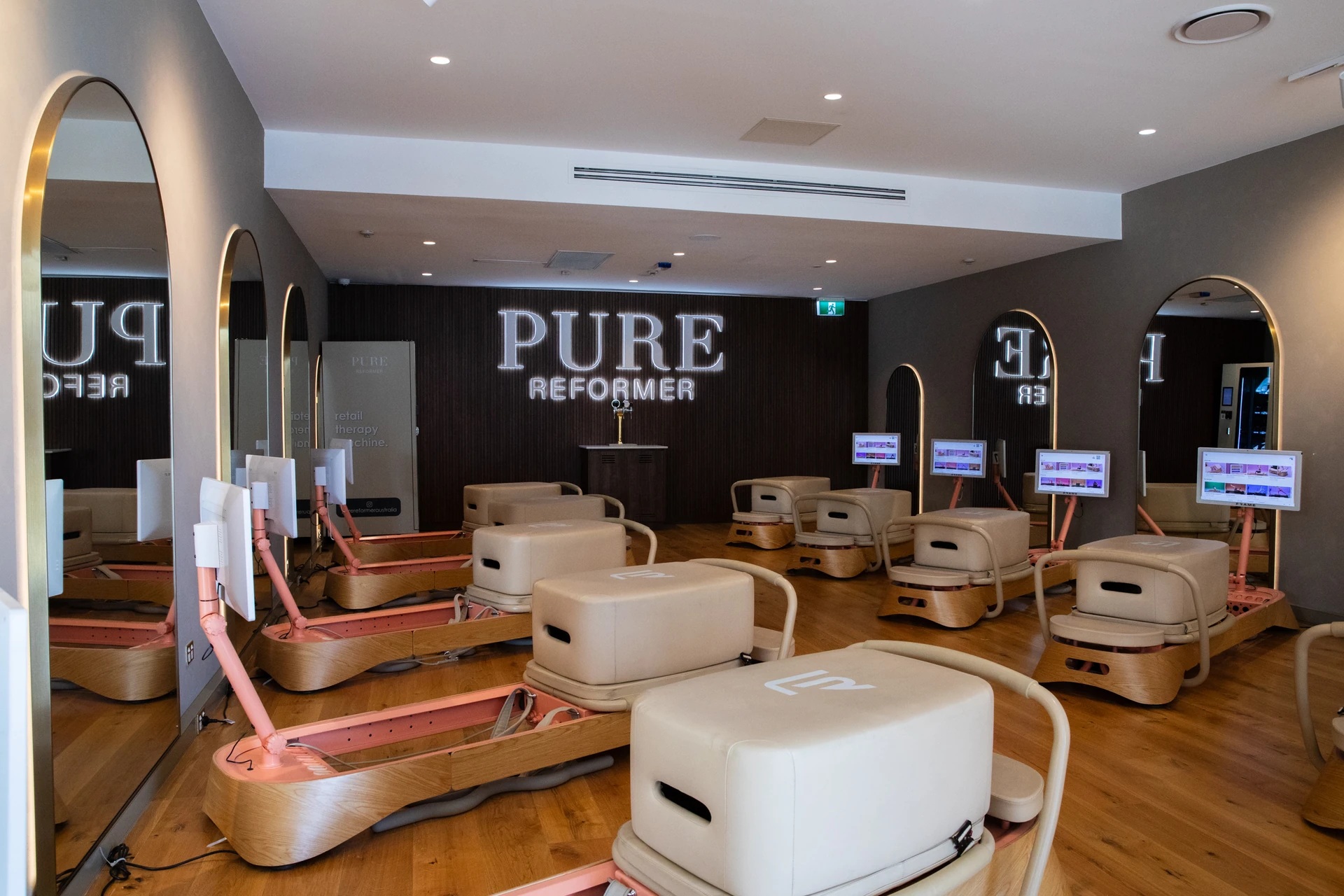 Reformers facing the illuminated Pure Reformer sign on a slatted feature wall